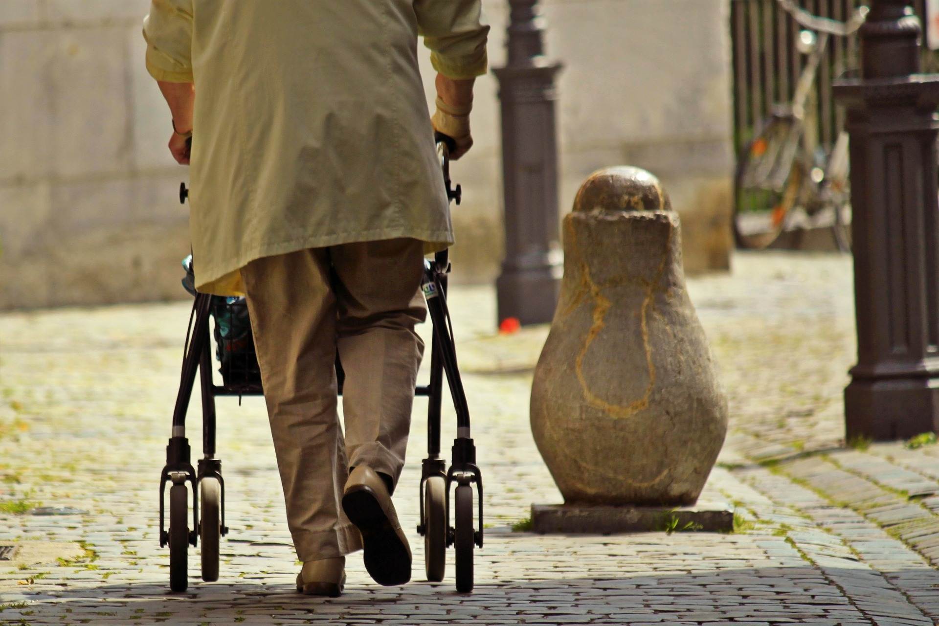 Ein älterer Mensch von hinten geht mit Rollator